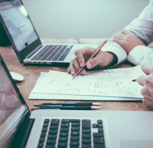 person holding pencil near laptop computer